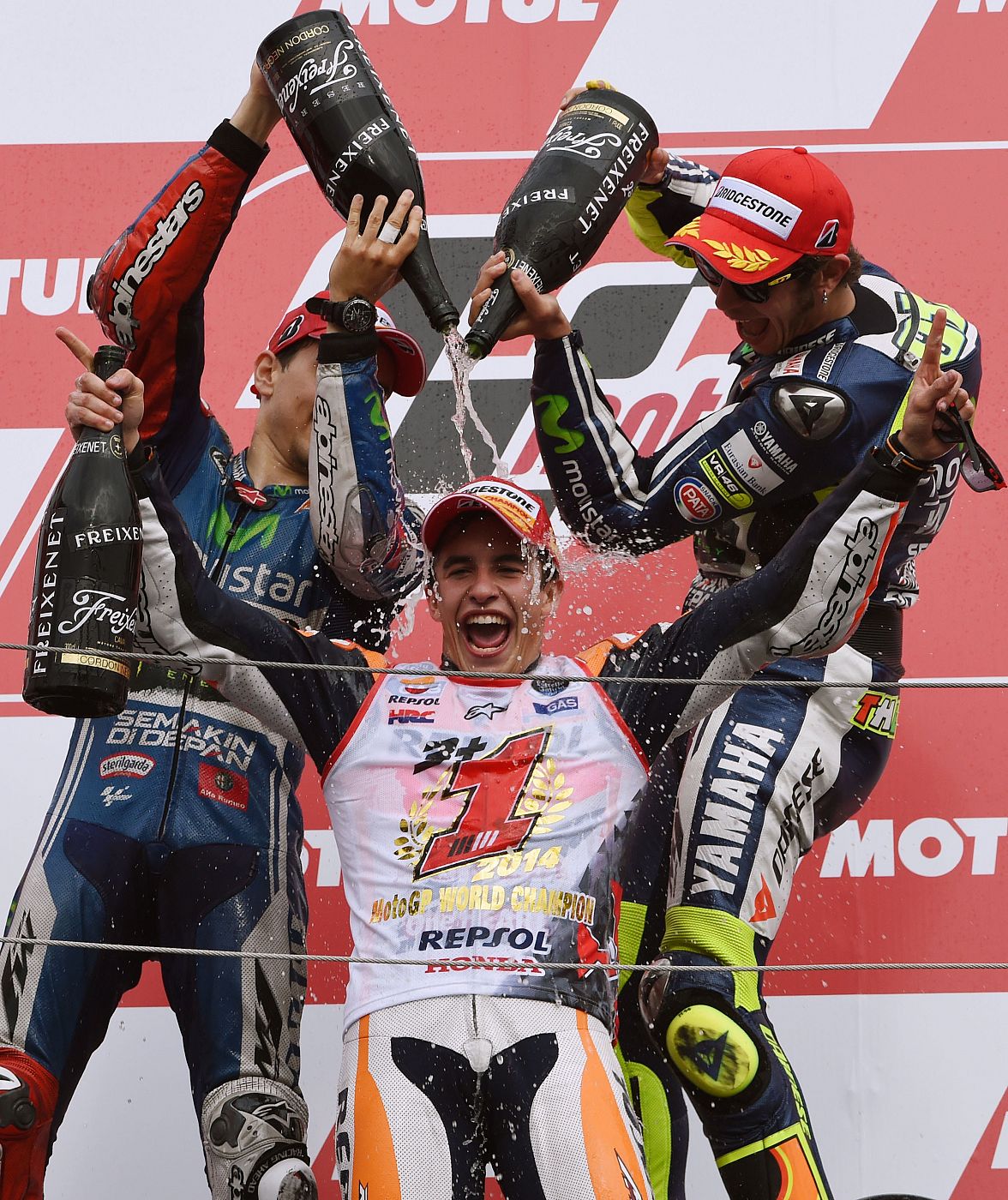 Márquez celebra su título en el podio, custodiado por Lorenzo y Rossi.