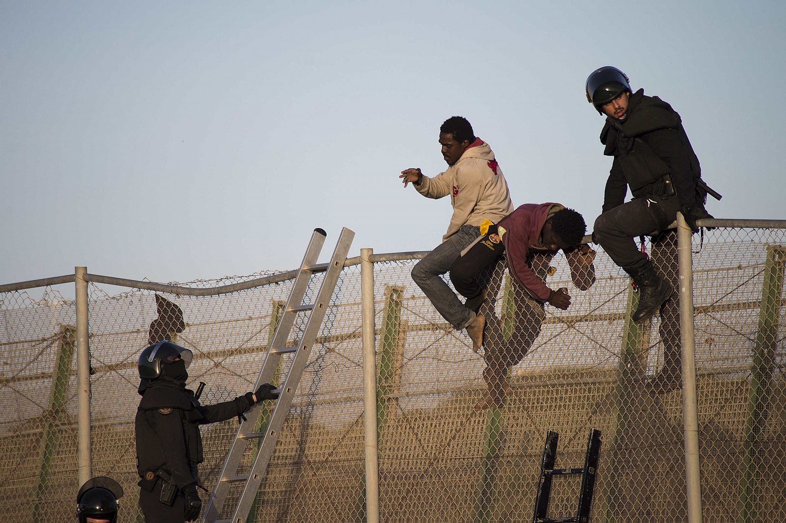 Antidisturbios españoles bajan a inmigrantes encaramados a la valla de Melilla