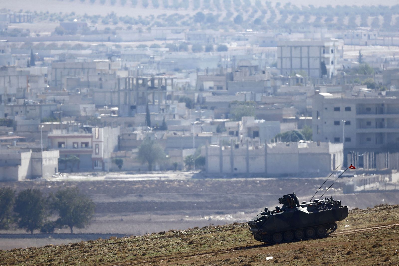 A Turkish army tank drives downhill, in front of ruins of the Syrian town of Kobani (seen in the background) near the Mursitpinar border crossing, on the Turkish-Syrian border, are seen in the background, near the southeastern town of Suruc in Sanliu