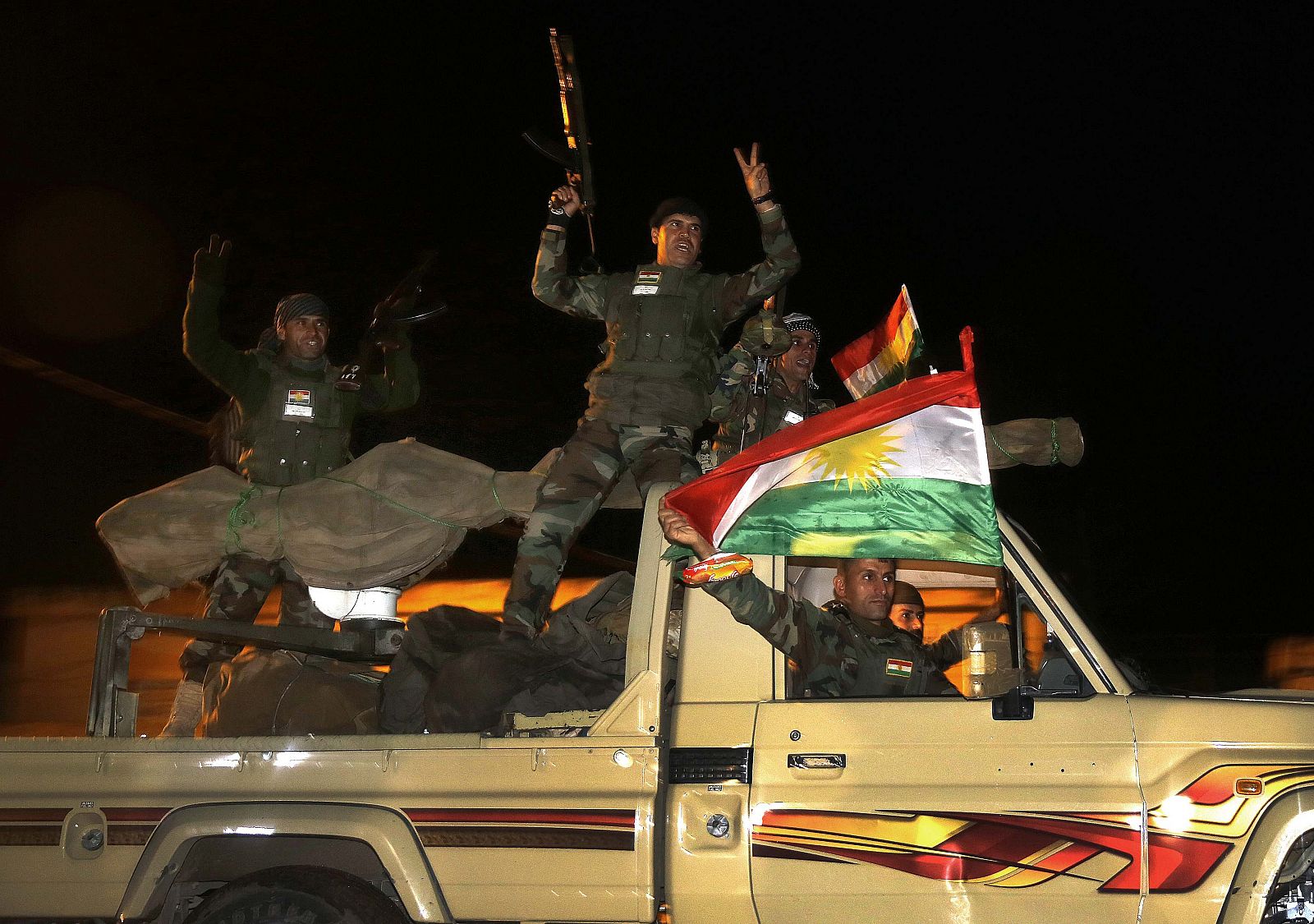 Kurdish peshmerga fighters wave flags as they move towards Kobani  from the Turkish town of Suruc
