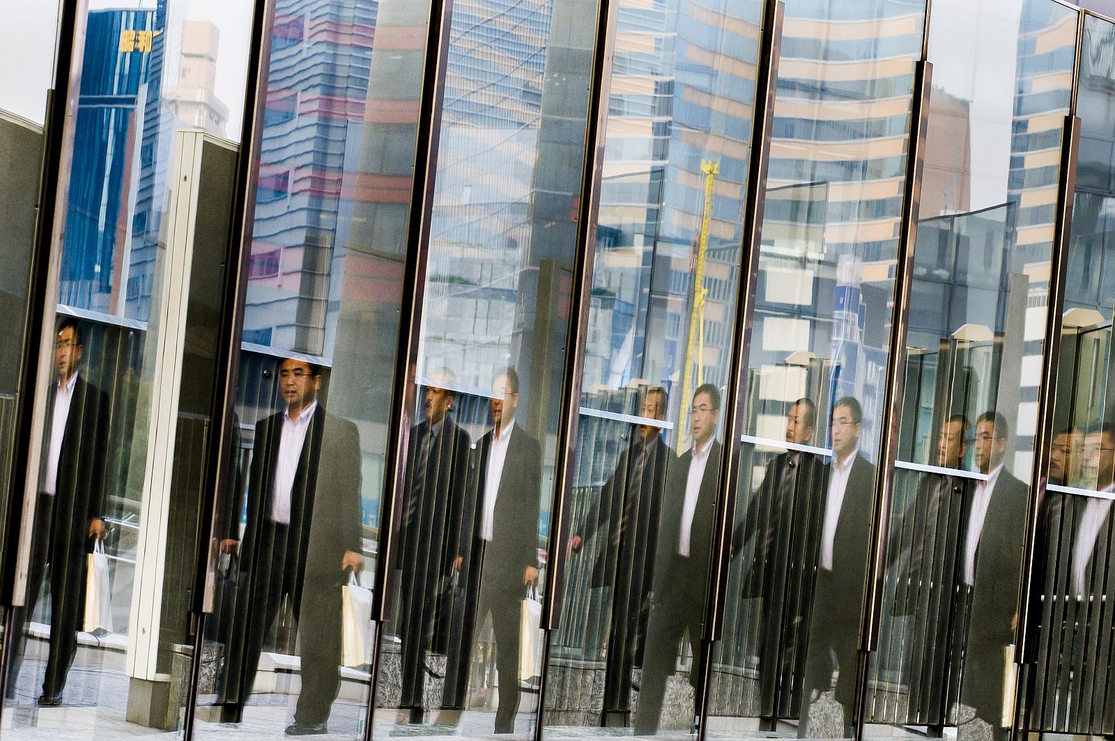 Un hombre se refleja en el cristal de un edificio del barrio de negocios de Tokio