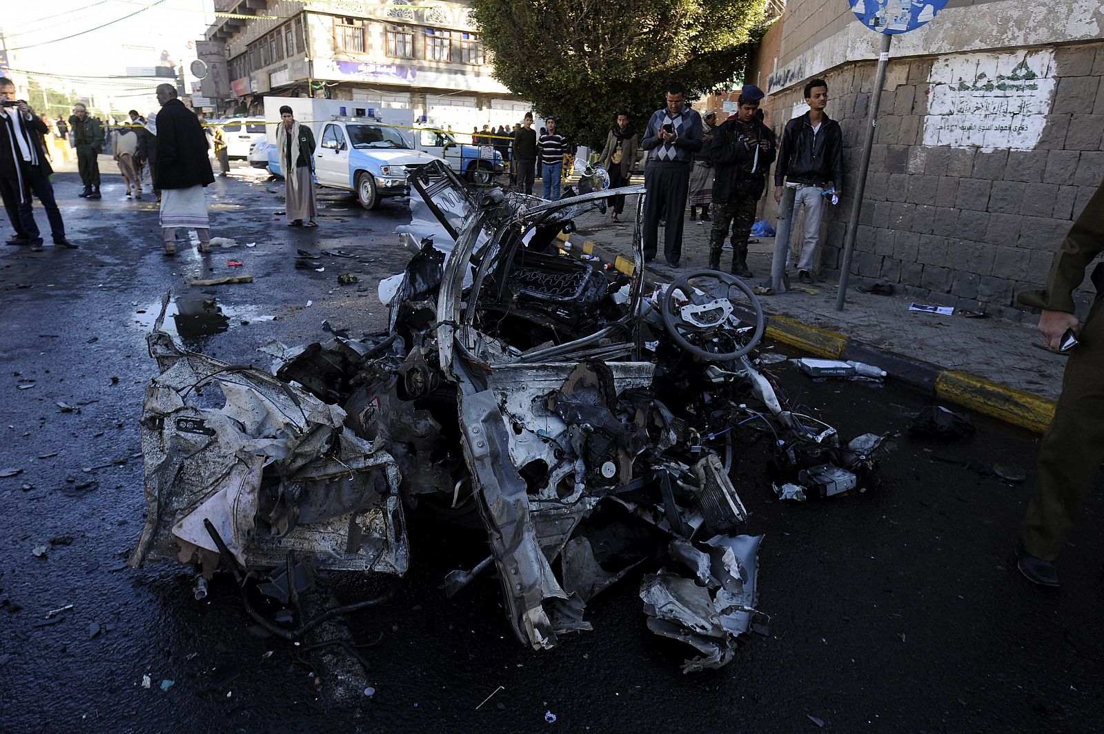 Yemeníes pasan junto a los restos del vehículo usado para un ataque suicida contra una academia de policía en Saná,