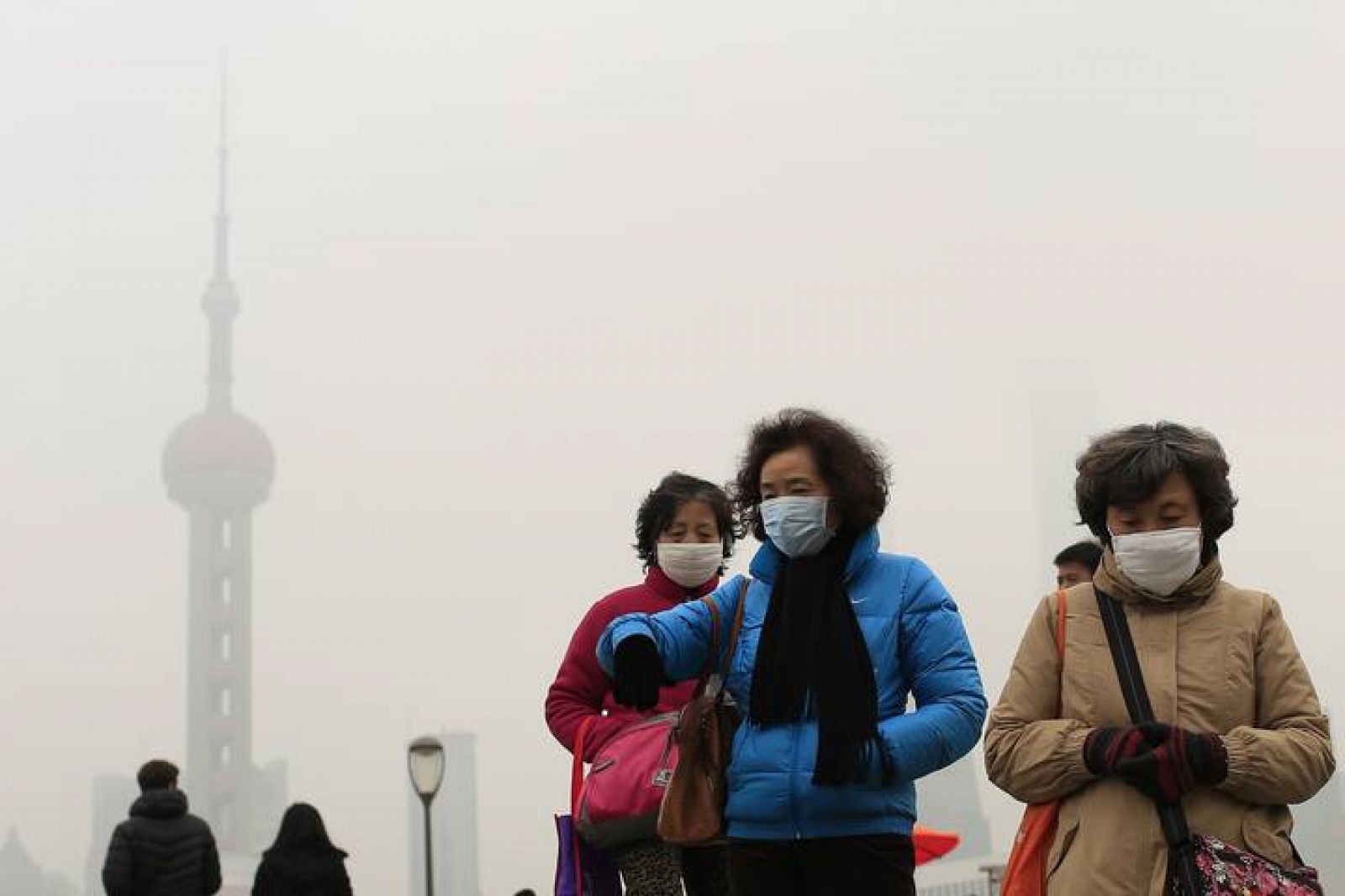 Varias mujeres con mascarilla, delante de la Torre de la Televisión de Shanghai