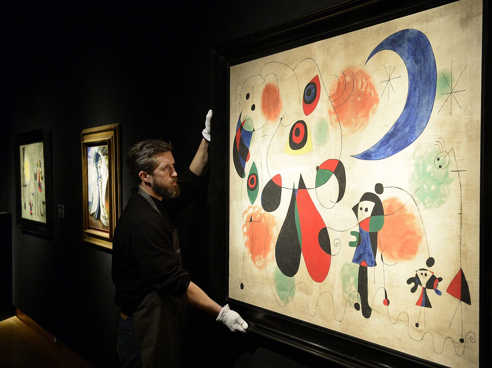 Un trabajador posa junto a la obra 'Mujeres, Luna, Pájaros', del artista español Joan Miró, en la casa de subastas Christie's, en Londres, Reino Unido.