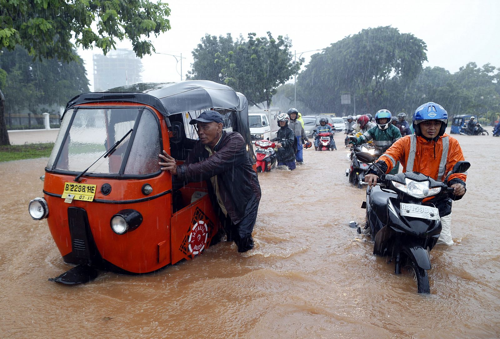 Un grupo de motoristas empuja sus vehículos en una calle inundada de Yakarta (Indonesia)
