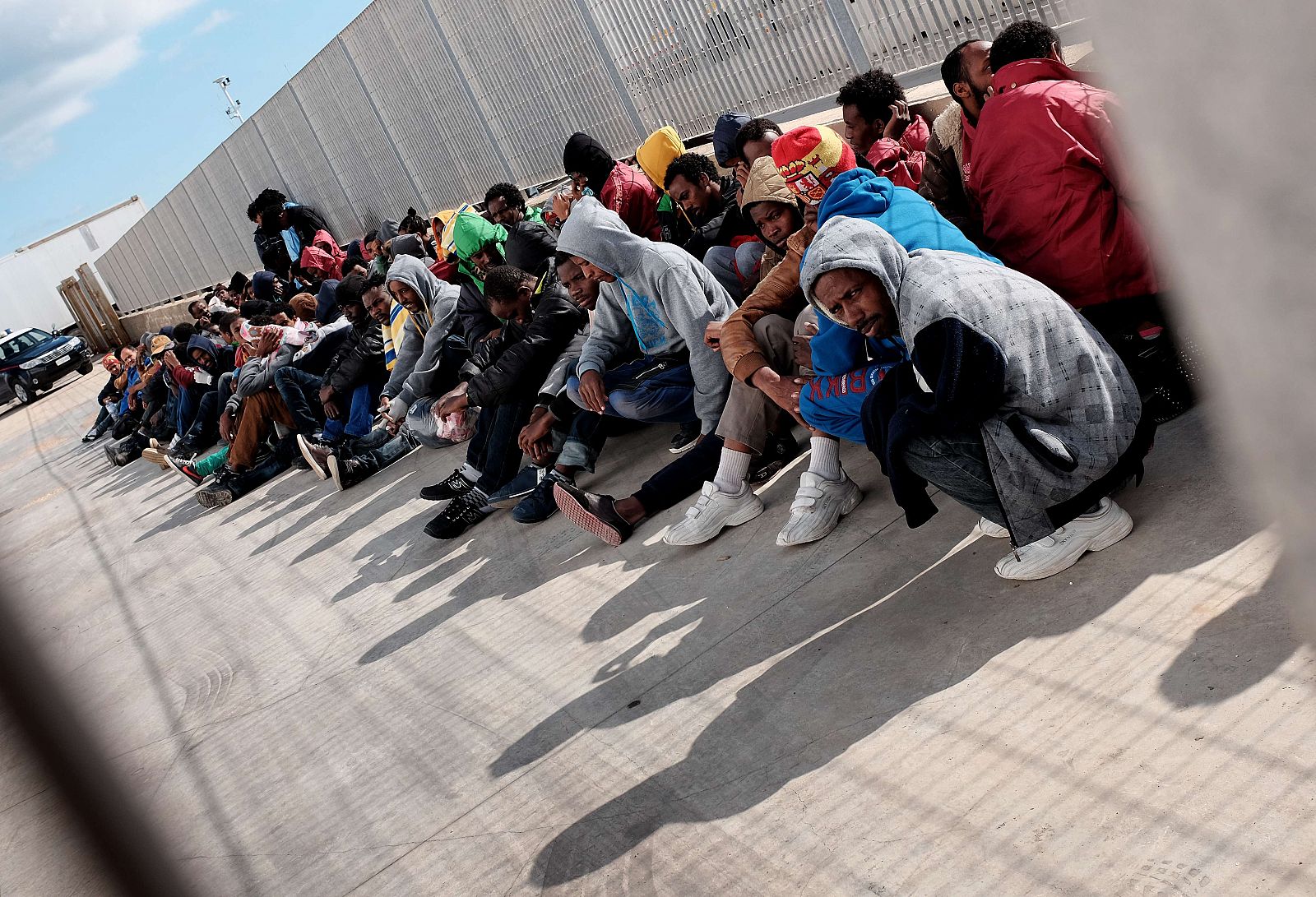 Un grupo de migrantes esperan en el puerto de Lampedusa la llegada del ferry que les llevará a Porto Empedocle en Sicilia
