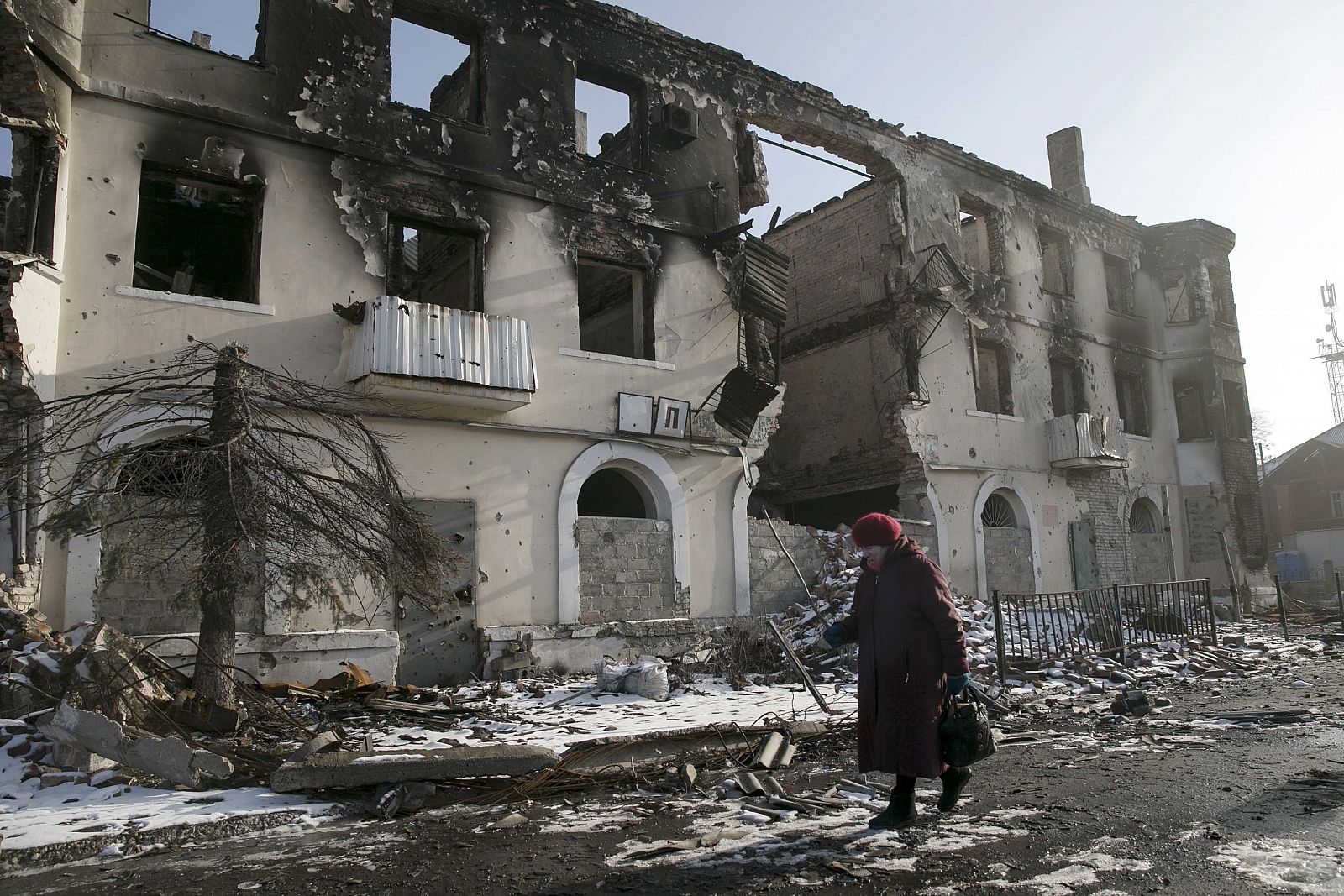 A woman walks past a damaged building in the town of Vuhlehirsk near Donetsk