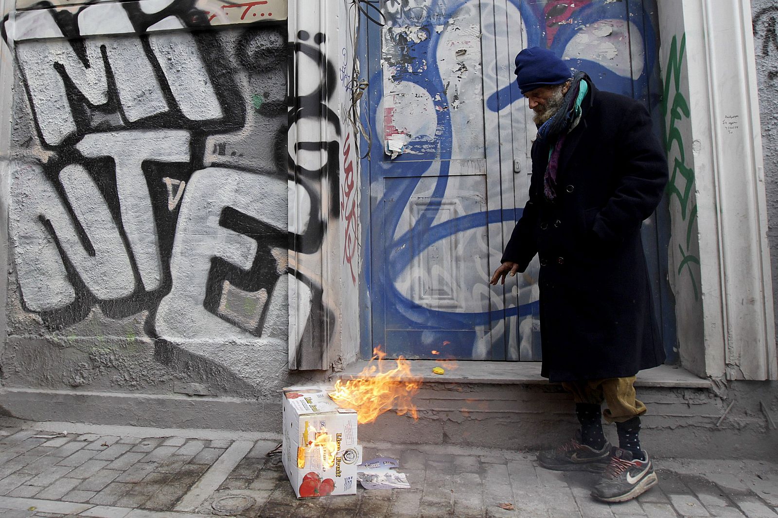 Una persona sin techo se calienta en una pequeña hoguera improvisada en Atenas.