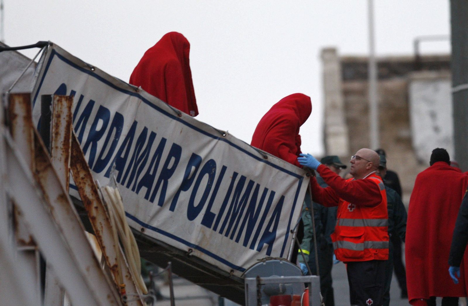 Un miembro de Cruz Roja junto a varios de los 26 inmigrantes que han llegado al puerto pesquero de Almería tras ser rescatados por Salvamento Marítimo en una patera la isla de Alborán.