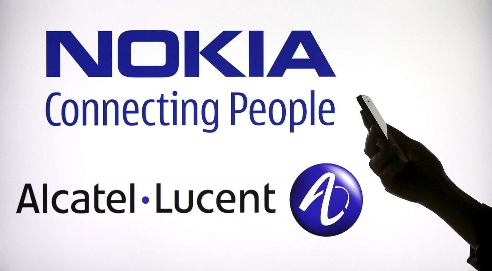 Una mujer observa un móvil delante de una pantalla con los logos de Nokia y Alcatel Lucent