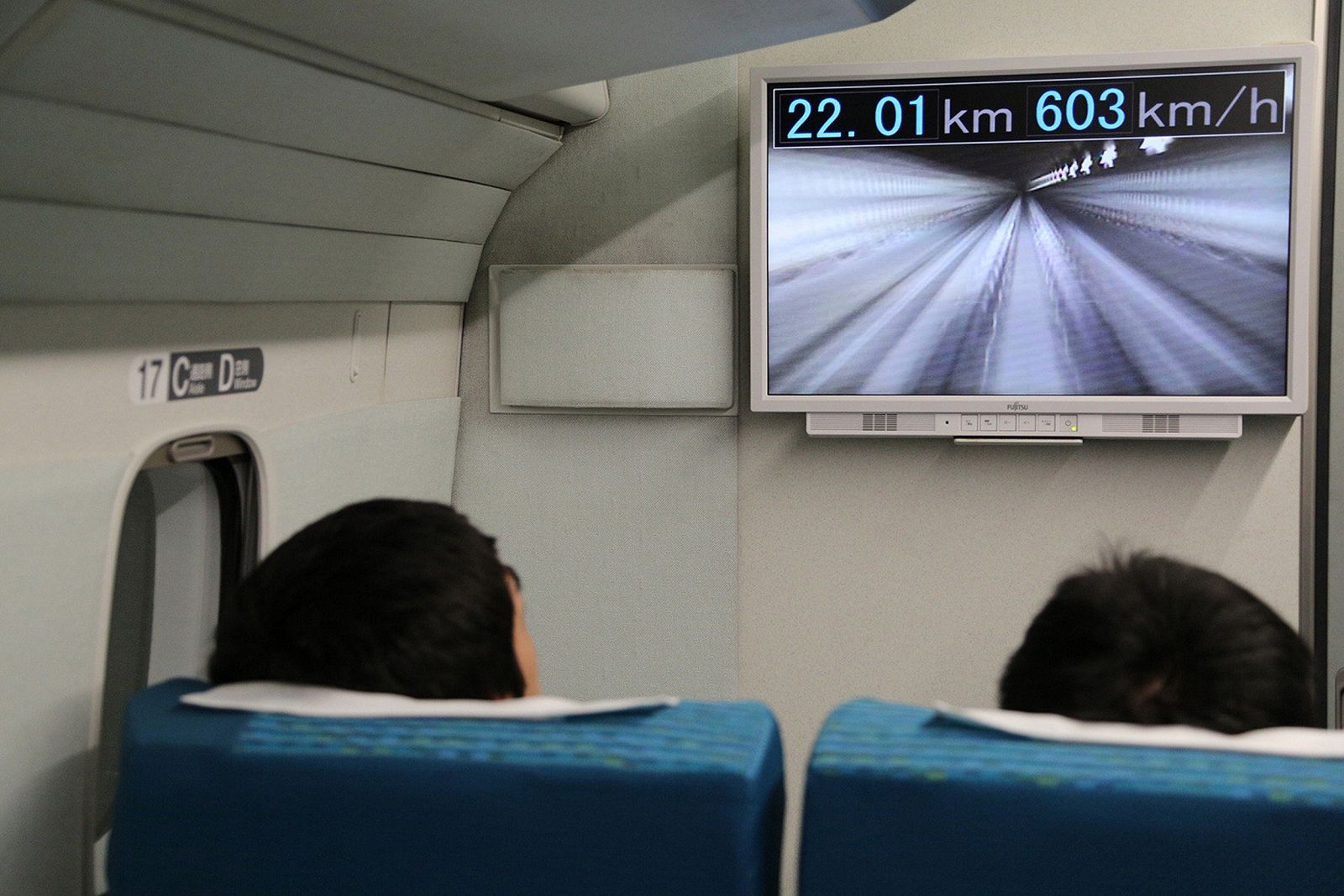 Pasajeros en el viaje de prueba del Maglev japonés observando la pantalla que marca 603 km/h de velocidad.