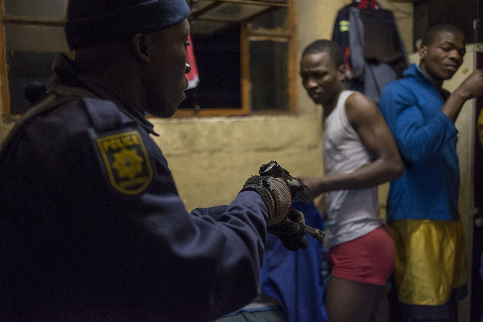 Un agente de la policía sudafricana apunta con su pistola a dos de los habitantes del albergue de trabajadores de Jeppestown, en Johanseburgo.