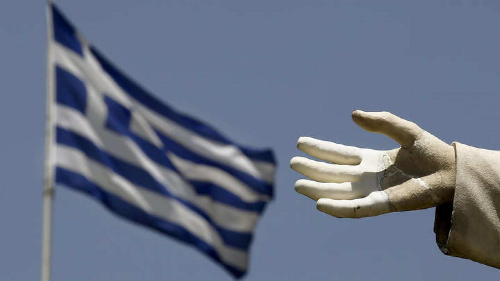La mano abierta de una estatua en primer plano y una bandera griega detrás