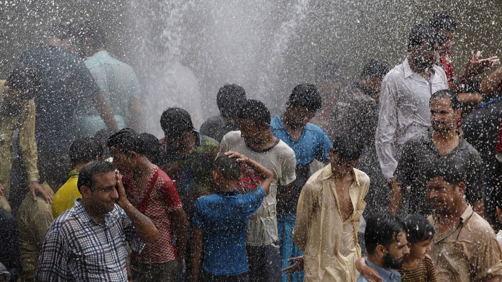 Un grupo de gente se refresca del calor en Karachi, Pakistán, con el agua de una tubería rota