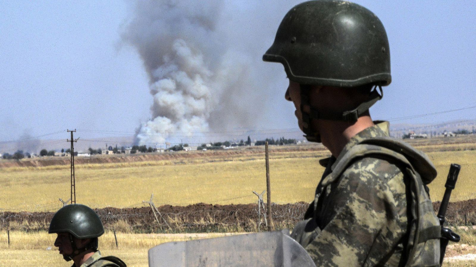 Soldados turcos montan guardia junto a la frontera con Siria, mientras al fondo columnas de humo se elevan sobre la ciudad de Kobani