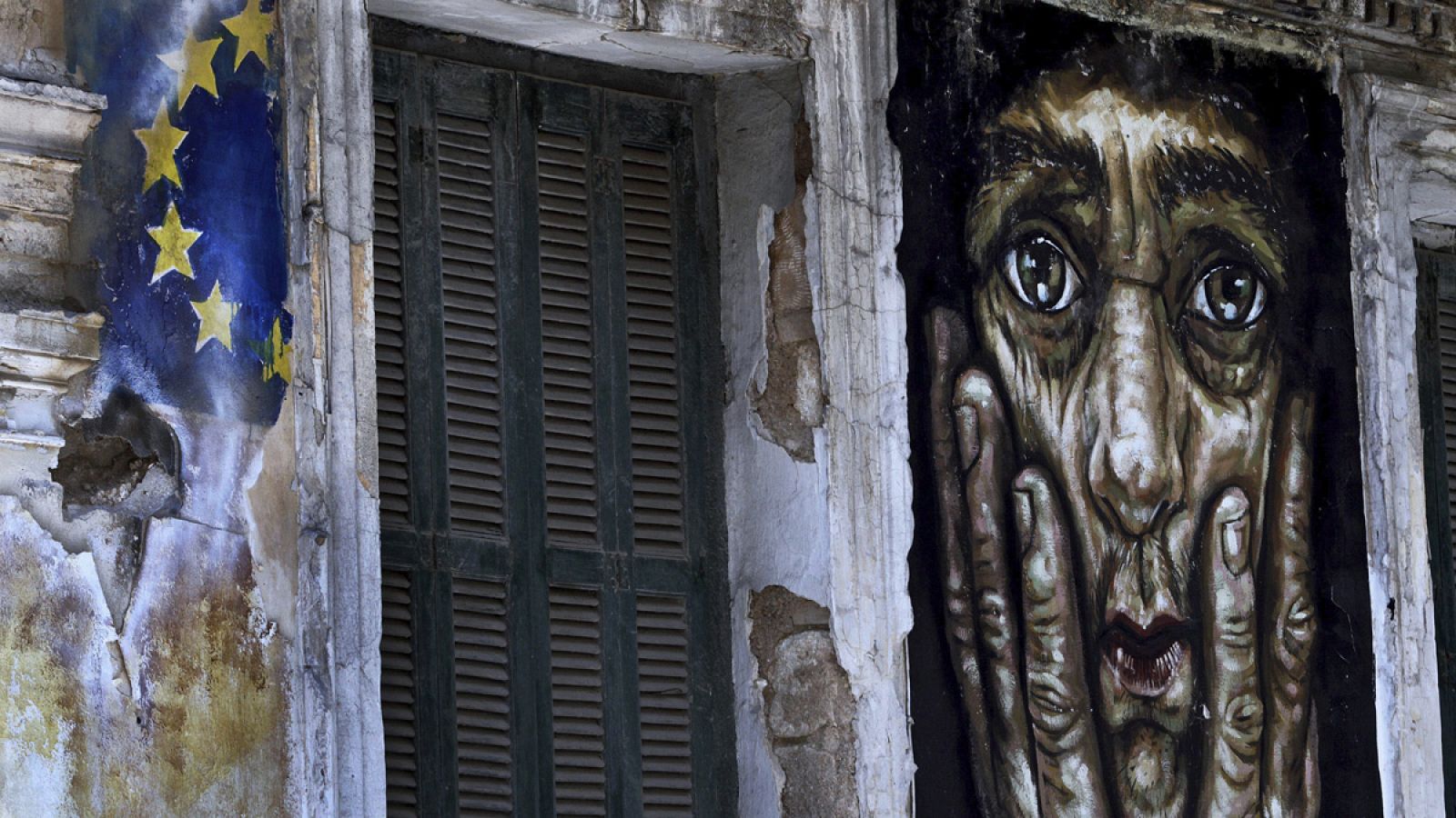 Pintada en un edificio de la bandera de la Unión Europea junto a un retrato en una pared de Atenas