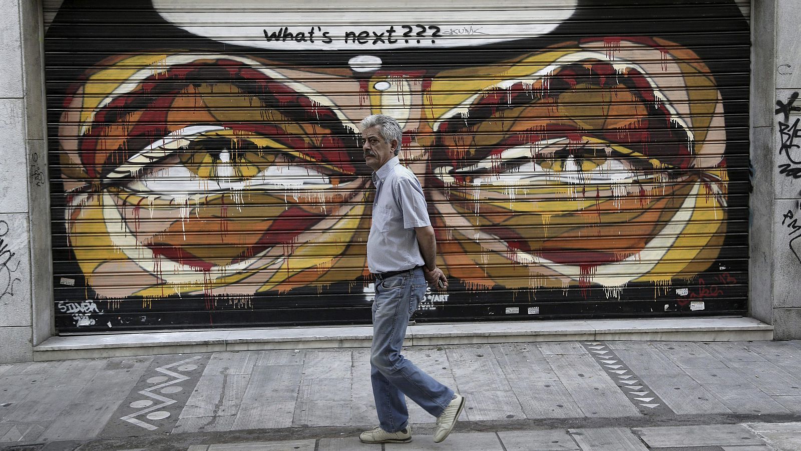 Un hombre pasa delante de un grafiti de un comercio en el centro de Atenas