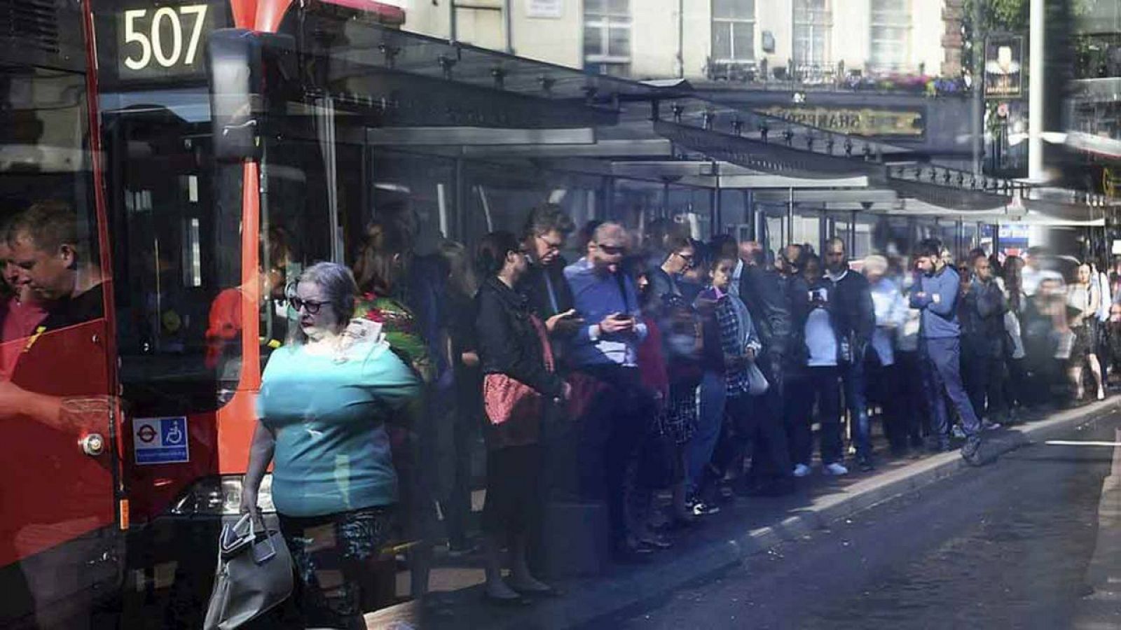 Reflejo, en una marquesina de una parada de un autobús, de los usuarios del transporte público que guardan largas colas para tomar un autobús
