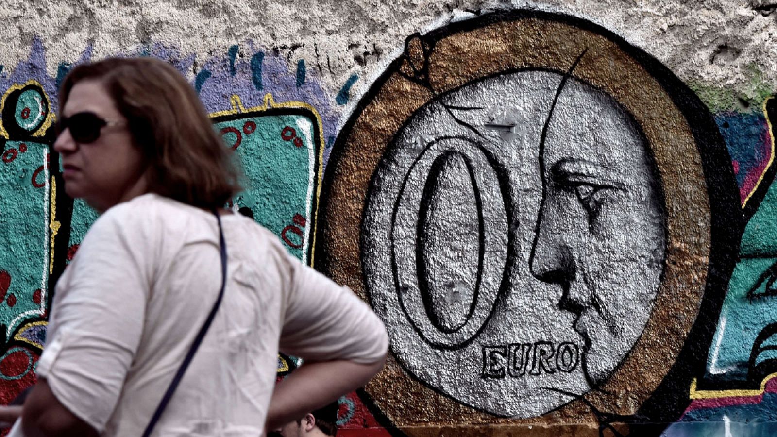 Una mujer, delante de un graffiti que muestra una moneda de cero euror en una calle del centro de Atenas