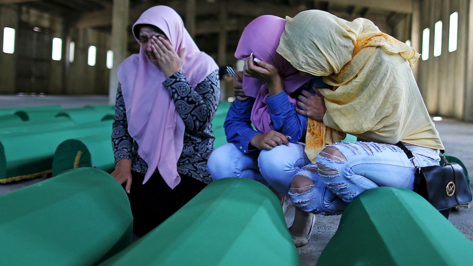Women cry next to coffins of their relatives who were victims of the 1995 Srebrenica massacre, at the Memorial Center in Potocari