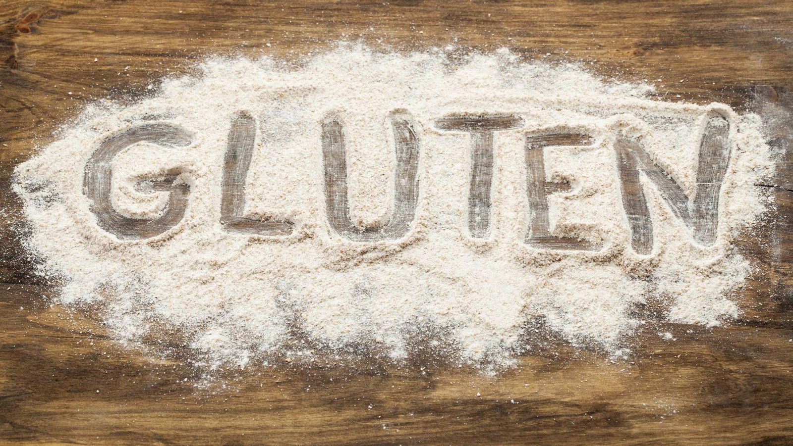 La palabra gluten dibujada en un montón de harina derramada en una mesa.