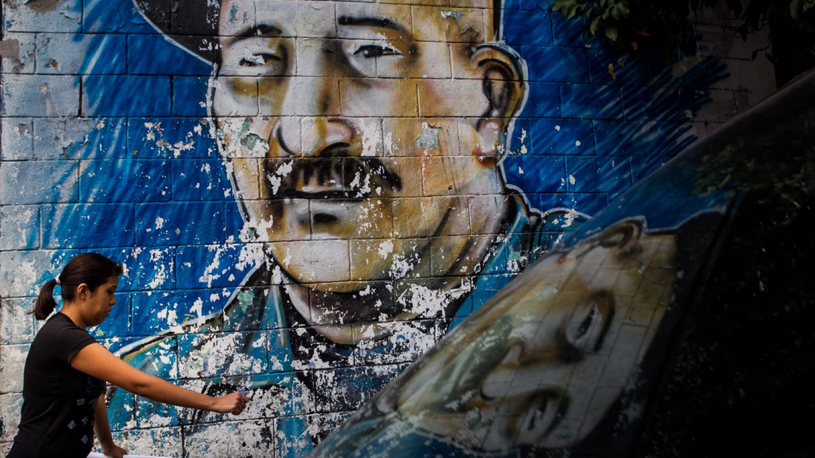 Una mujer camina frente al grafiti que muestra al fallecido líder guerrillero colombiano Víctor Julio Suárez