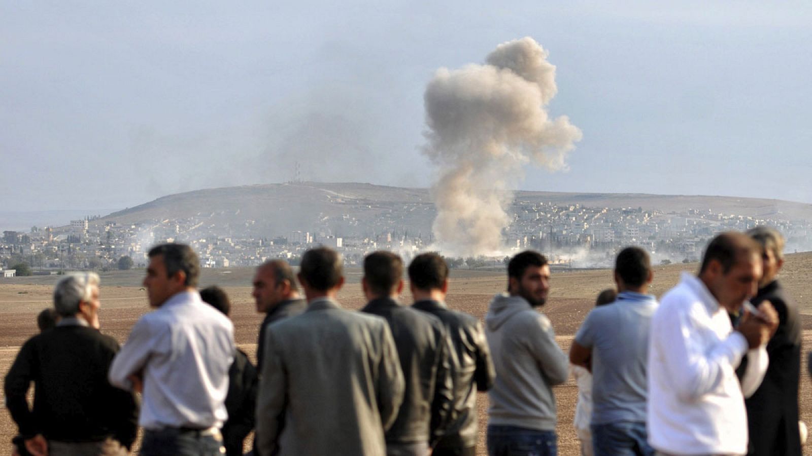Imagen de archivo de  unos hombres observando una columna de humo tras un  ataque de las fuerzas de la coalición lideradas por Estados Unidos en Siria.