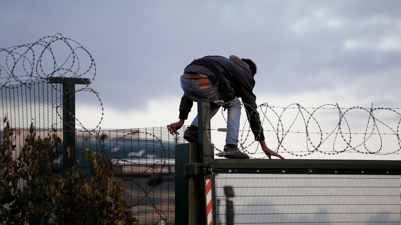 Un migrante salta una cerca antes de intentar tomar un tren en su ruta hacia Inglaterra, en Calais