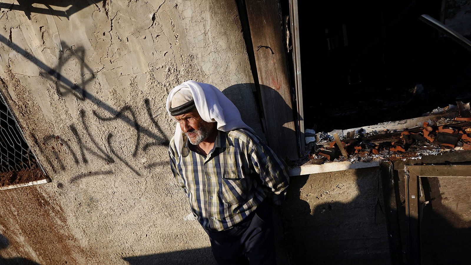 Un familiar de la víctima junto a la casa quemada en Douma, donde los atacantes han escrito "venganza" en hebreo