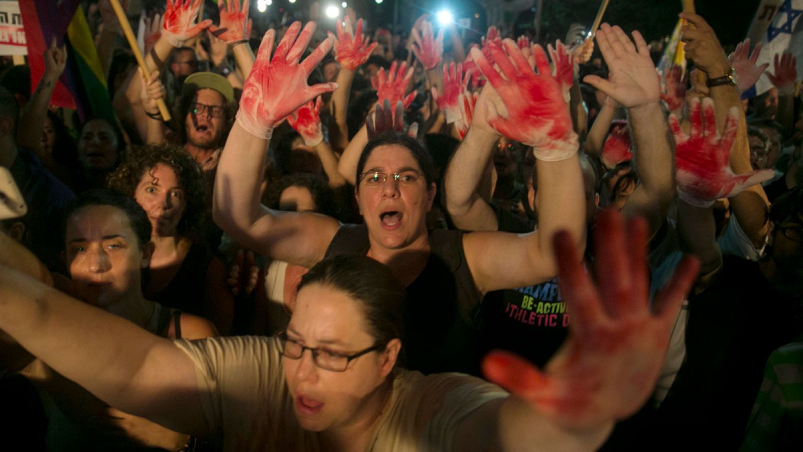 Manifestantes alzan sus manos con guantes manchados de guantes durante la manifestación contra el odio en Tel Aviv.