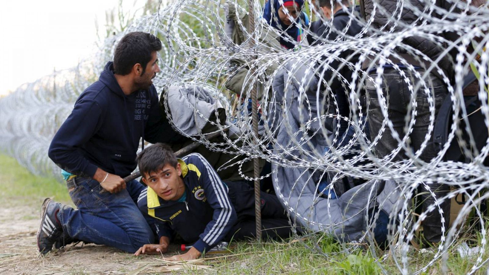 Refugiados sirios cruzan hacia Hungría bajo la alambrada metálica desplegada en la frontera con Serbia.