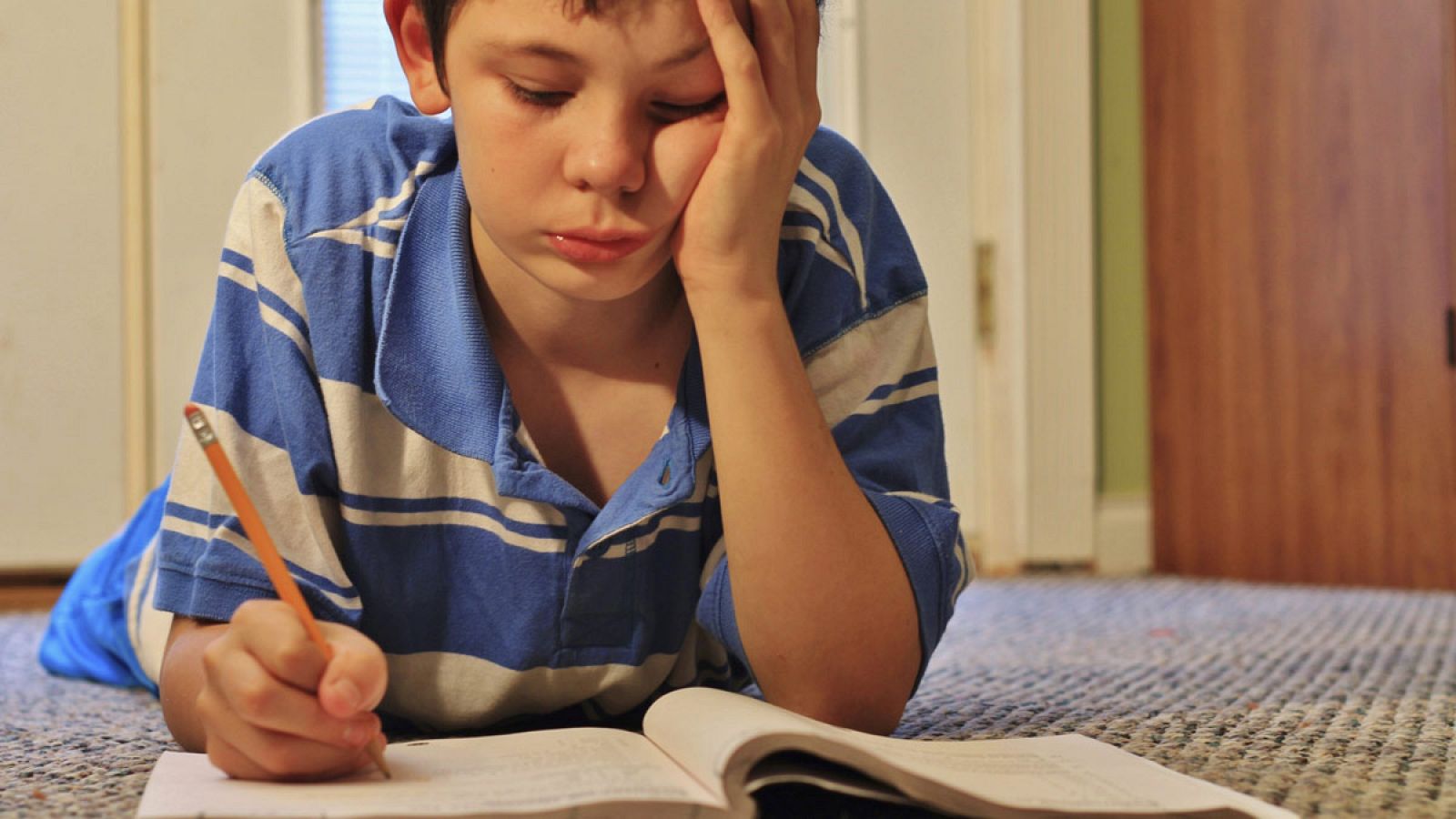 Un niño haciendo deberes con un libro en el suelo