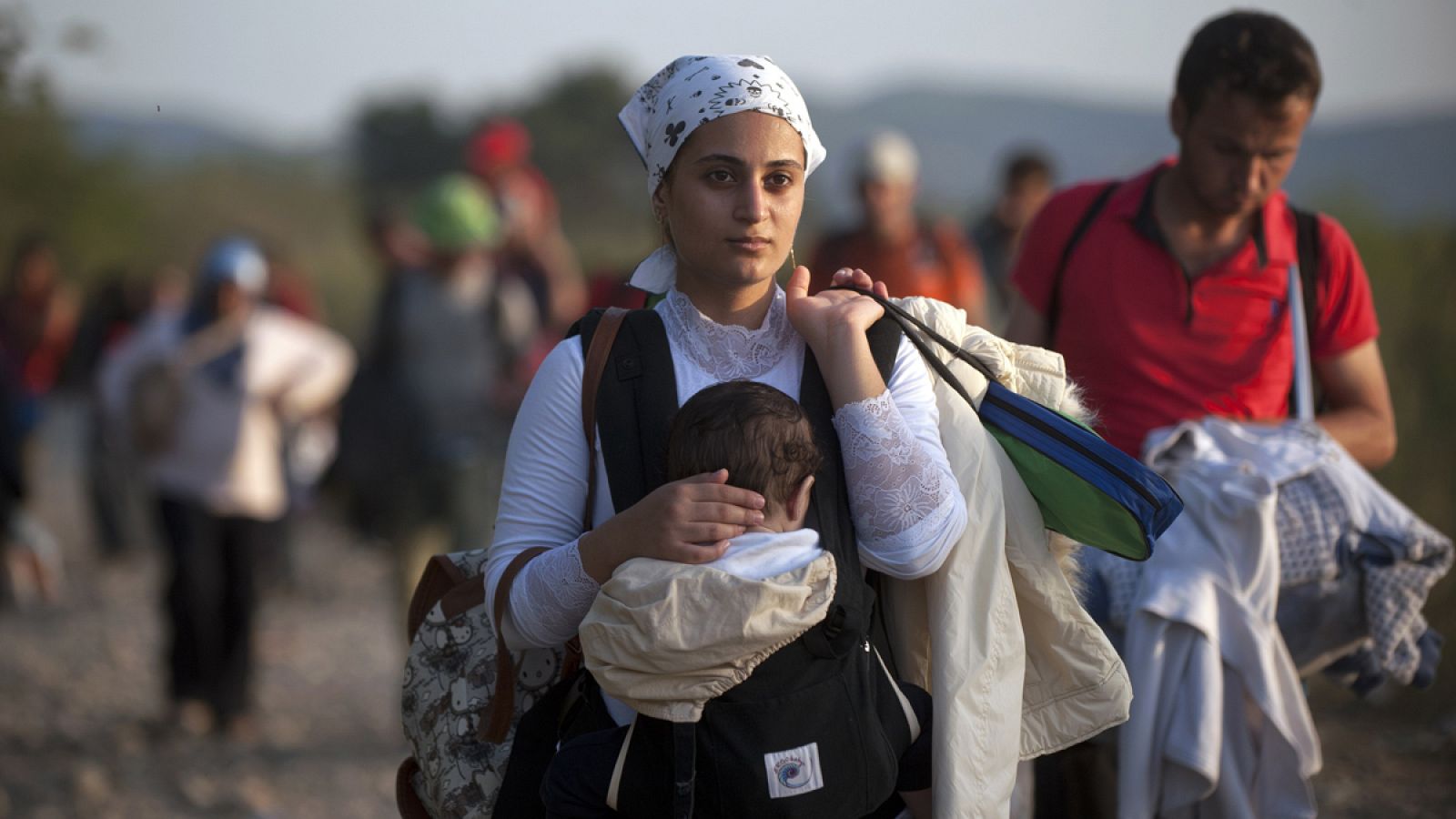 Una mujer refugiada carga con su hijo en la isla de Macedonia