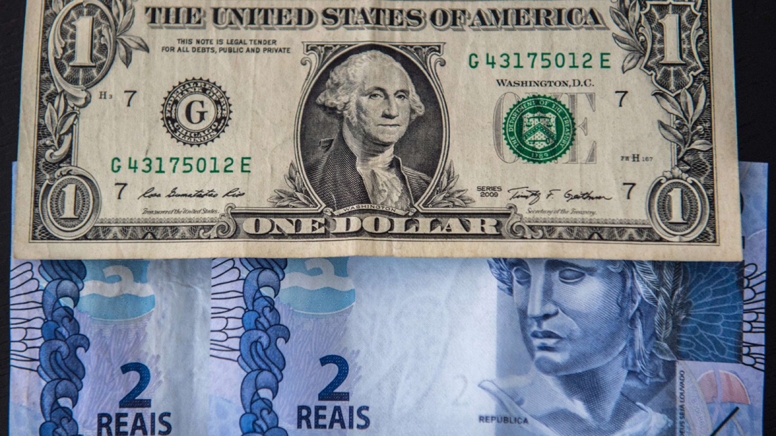 Un billete de un dólar junto a dos billetes de dos reales