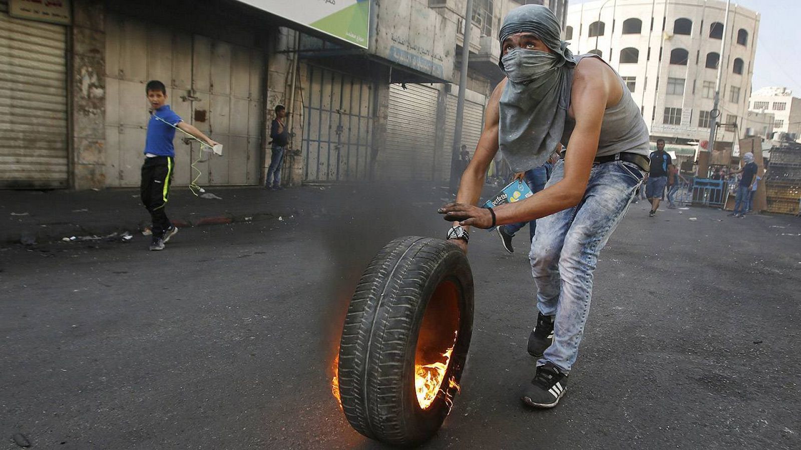 Un palestino empuja un neumático ardiendo durante los enfrentamientos con las fuerzas de seguridad israelíes en Hebrón, sur de Cisjordania, el 4 de octubre de 2015. REUTERS/Mussa Qawasma  