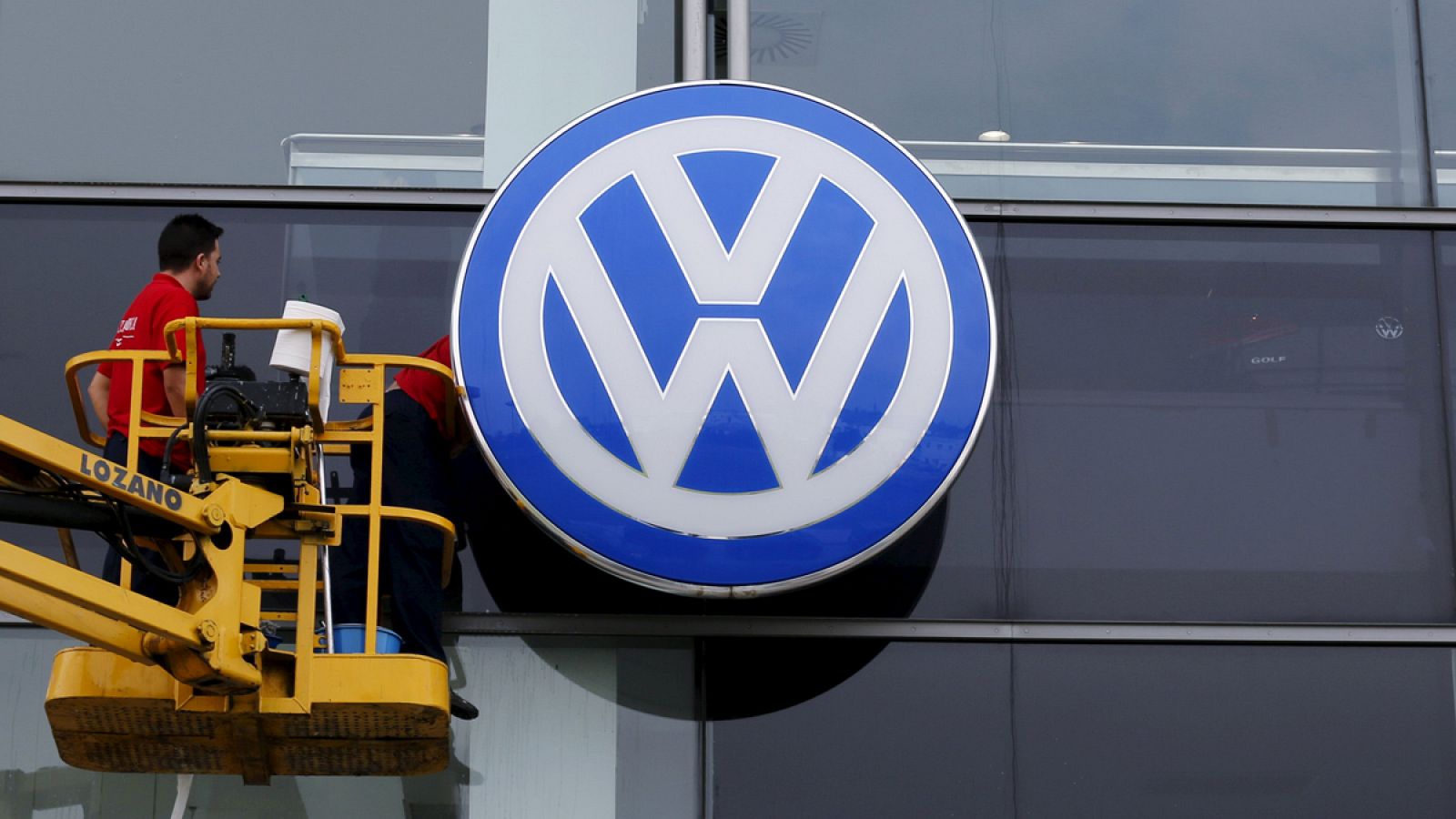 Dos trabajadores limpian la fachada de una sede de Volkswagen en Sevilla