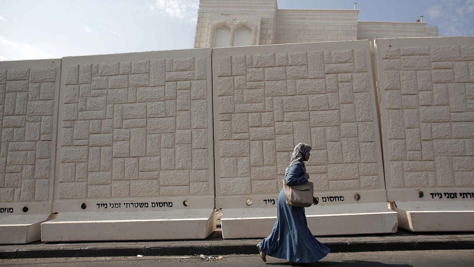 Una mujer palestina pasa junto a uno de los muros de cemento erigidos por la Policía israelí en el barrio de Yabal Mukaber, en Jerusalén Este. En el muro, en hebreo, se puede leer: "Barrera policial de separación temporal"