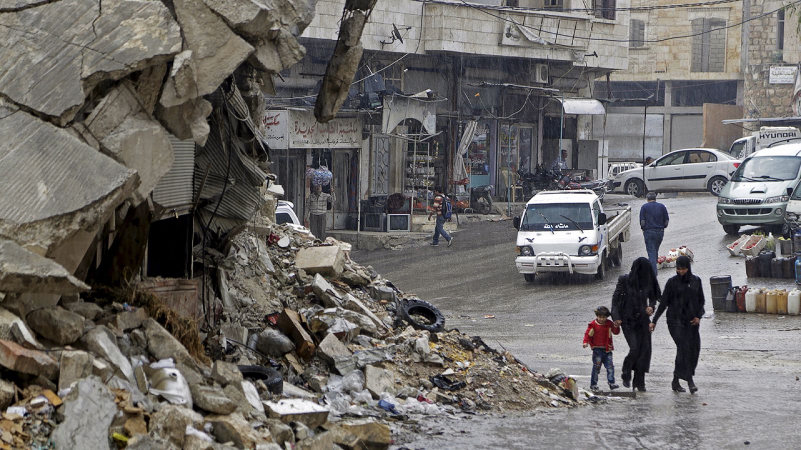 Civiles caminan bajo la lluvia junto a un edificio destruido en el pueblo de Maaret al Numan, en Siria