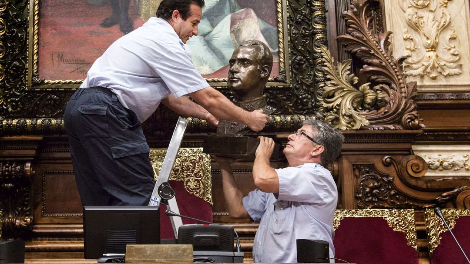 Dos operarios retiran el busto del rey del salón de plenos municipales del Ayuntamiento de Barcelona.