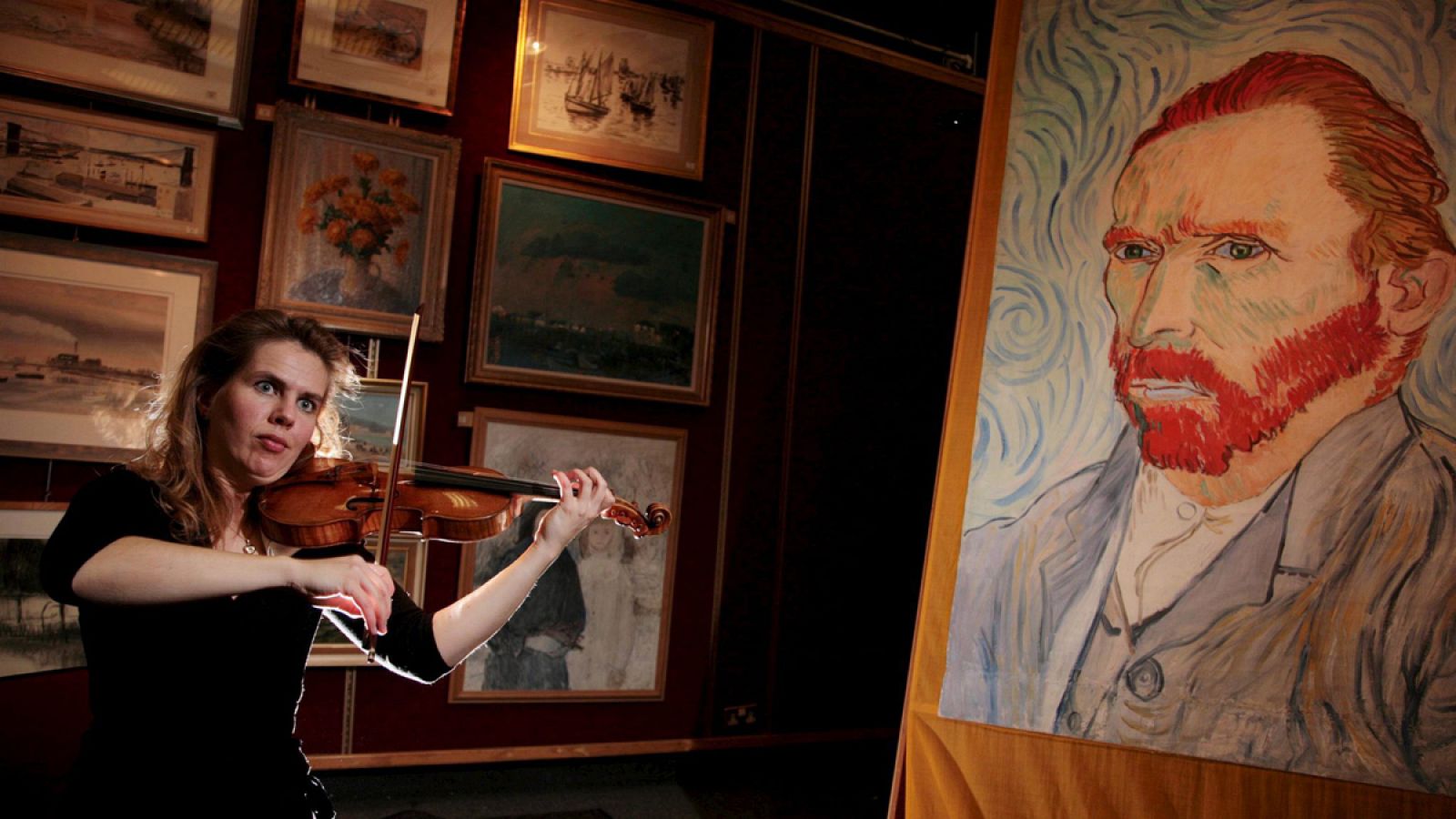Una mujer toca el violín delante de un autorretrato de Van Gogh.