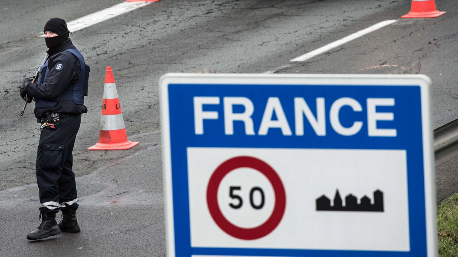 Un policía armado vigila mientras otro comprueba la documentación de varios conductores en la frontera franco-belga