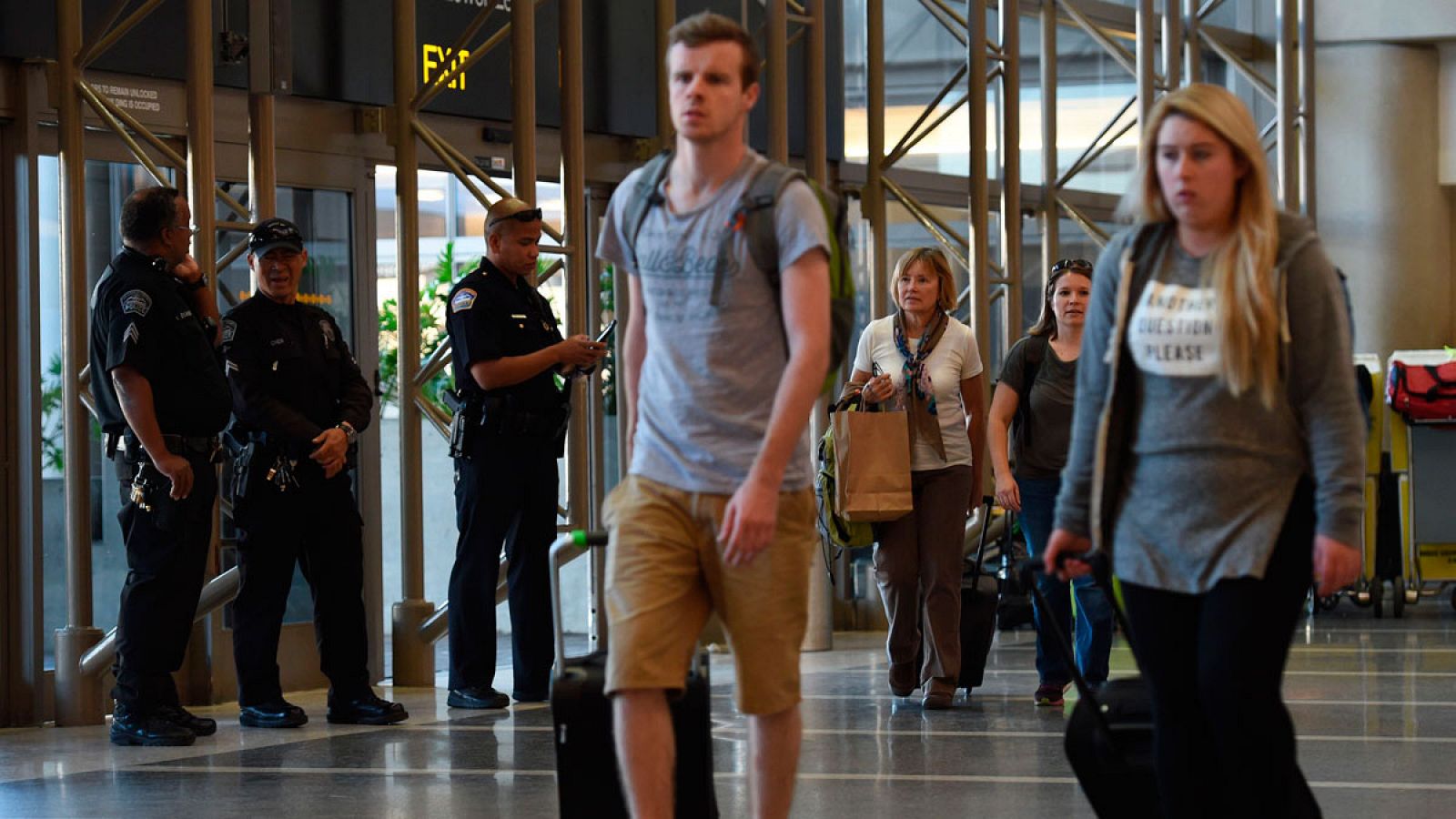 Varios pasajeros en el aeropuerto internacional de Los Ángeles caminan entre policías y fuerzas de seguridad.
