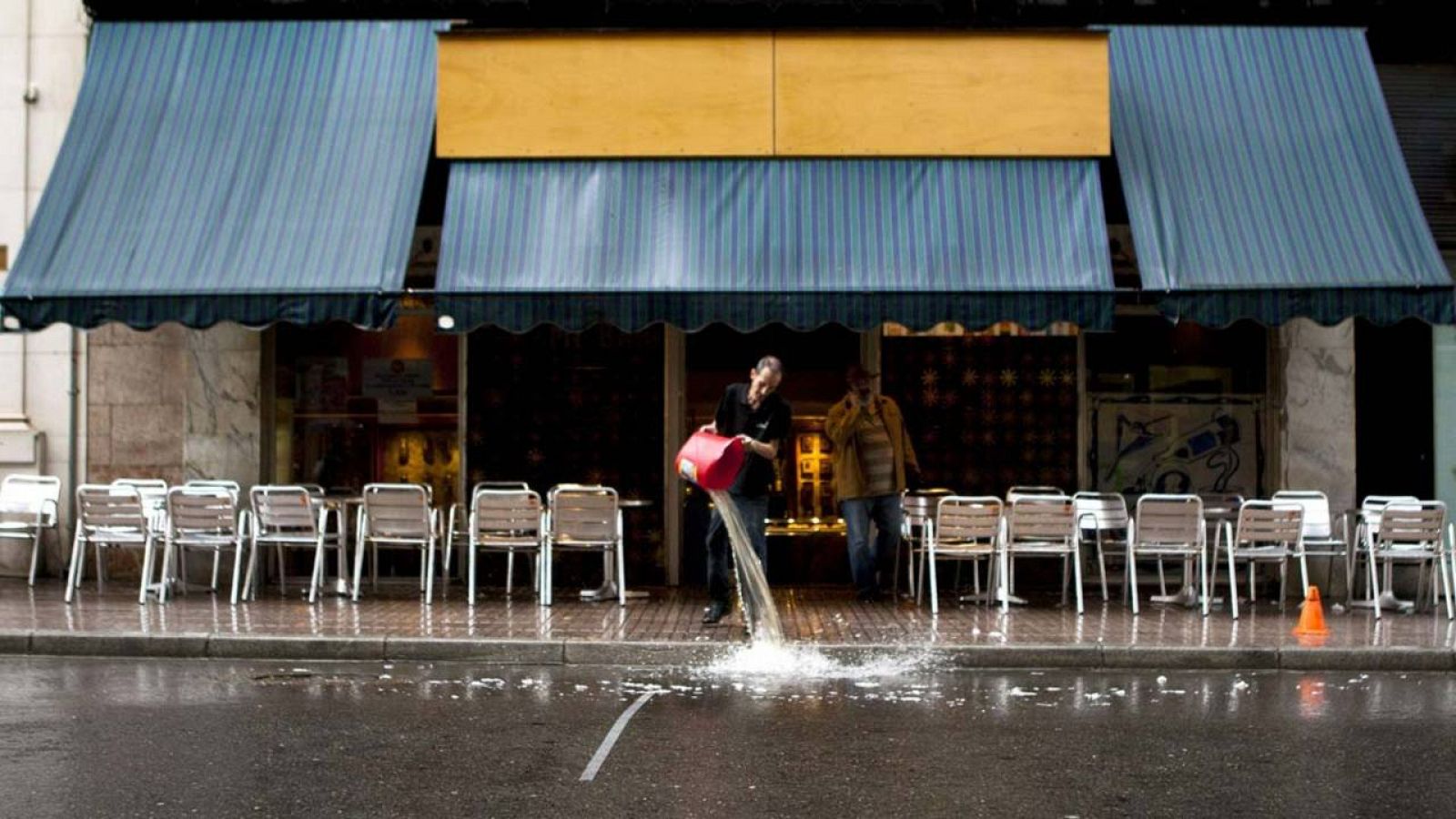 Un trabajador vacía un cubo de agua a la puerta de un bar en Huesca