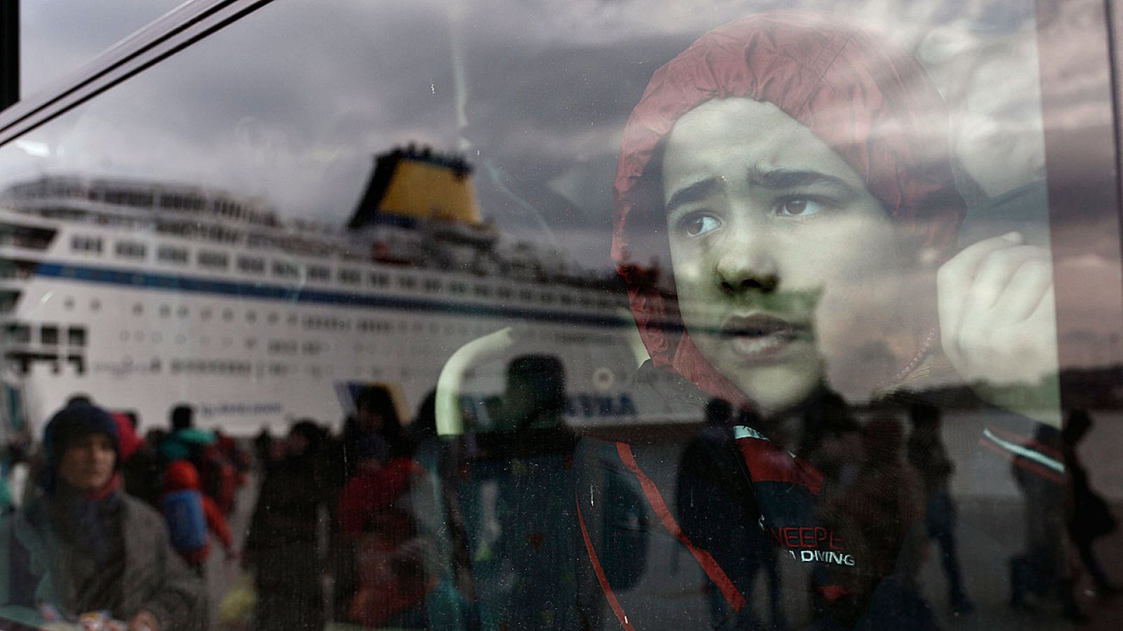 Un niño refugiado mira a través del autobús el ferry en el que ha llegado al puerto de Atenas con otros 2.500 migrantes.