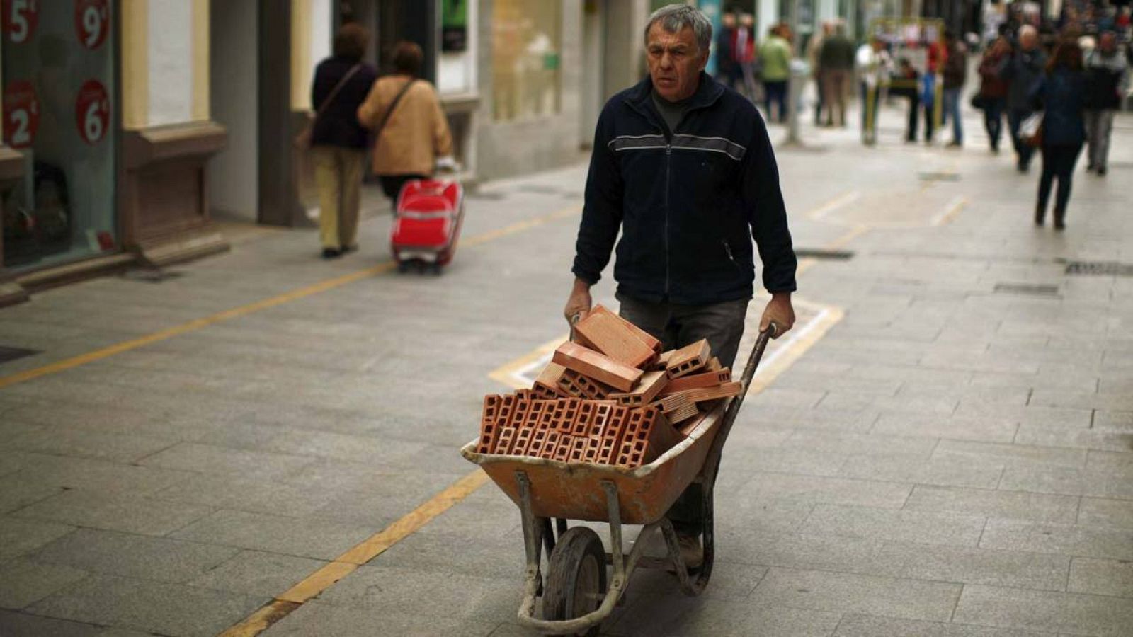 Un trabajador de la construcción lleva un carretillo de ladrillos por una calle de Ronda