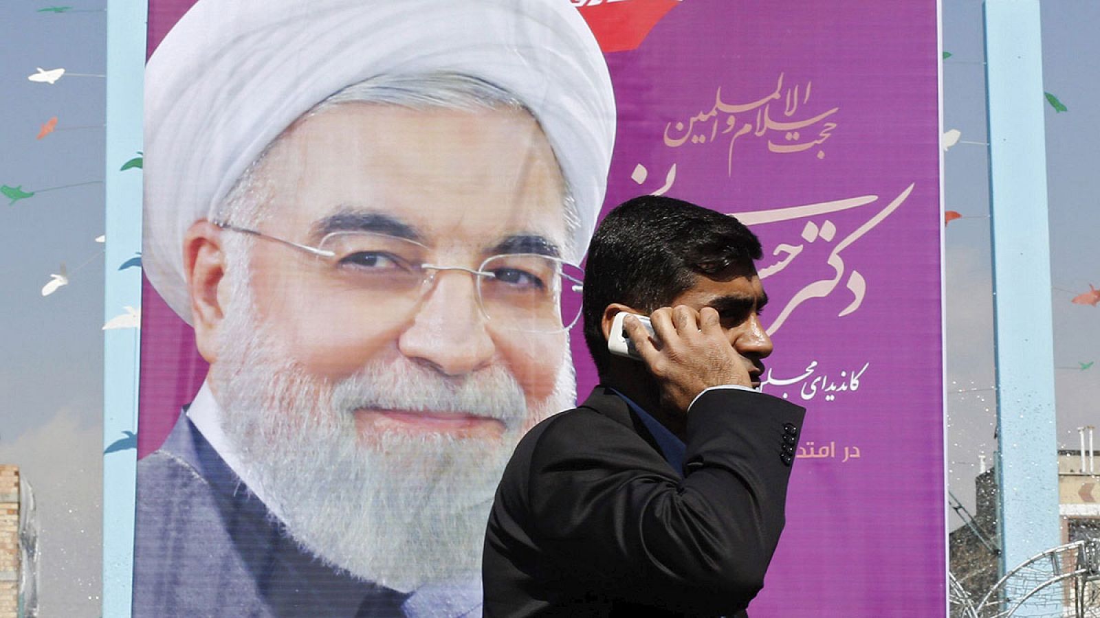 Un hombre camina junto a un cartel electoral de Hasan Rohani en Teherán