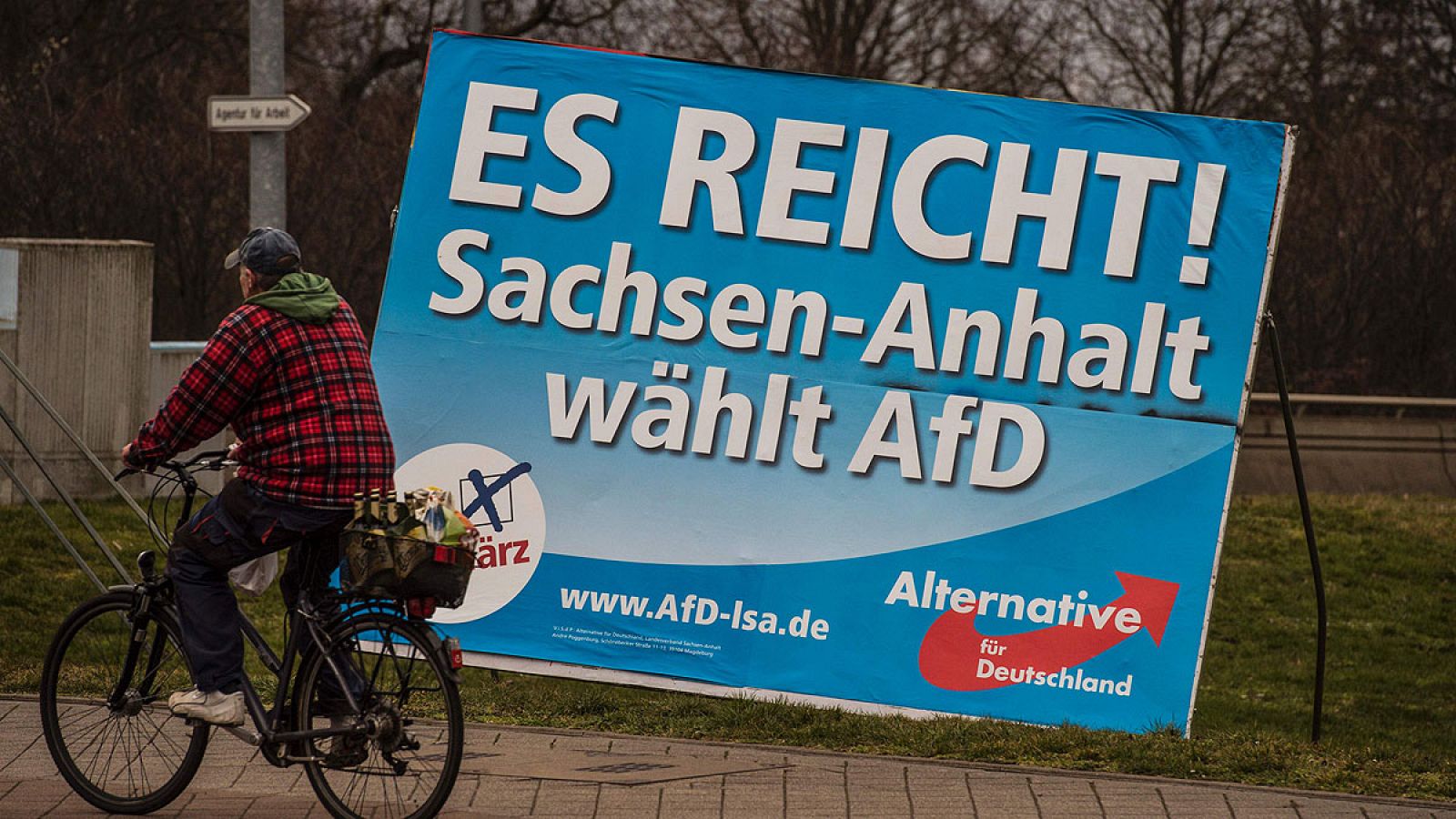 Un hombre en bicicleta pasa junto a un cartel electoral de AfD