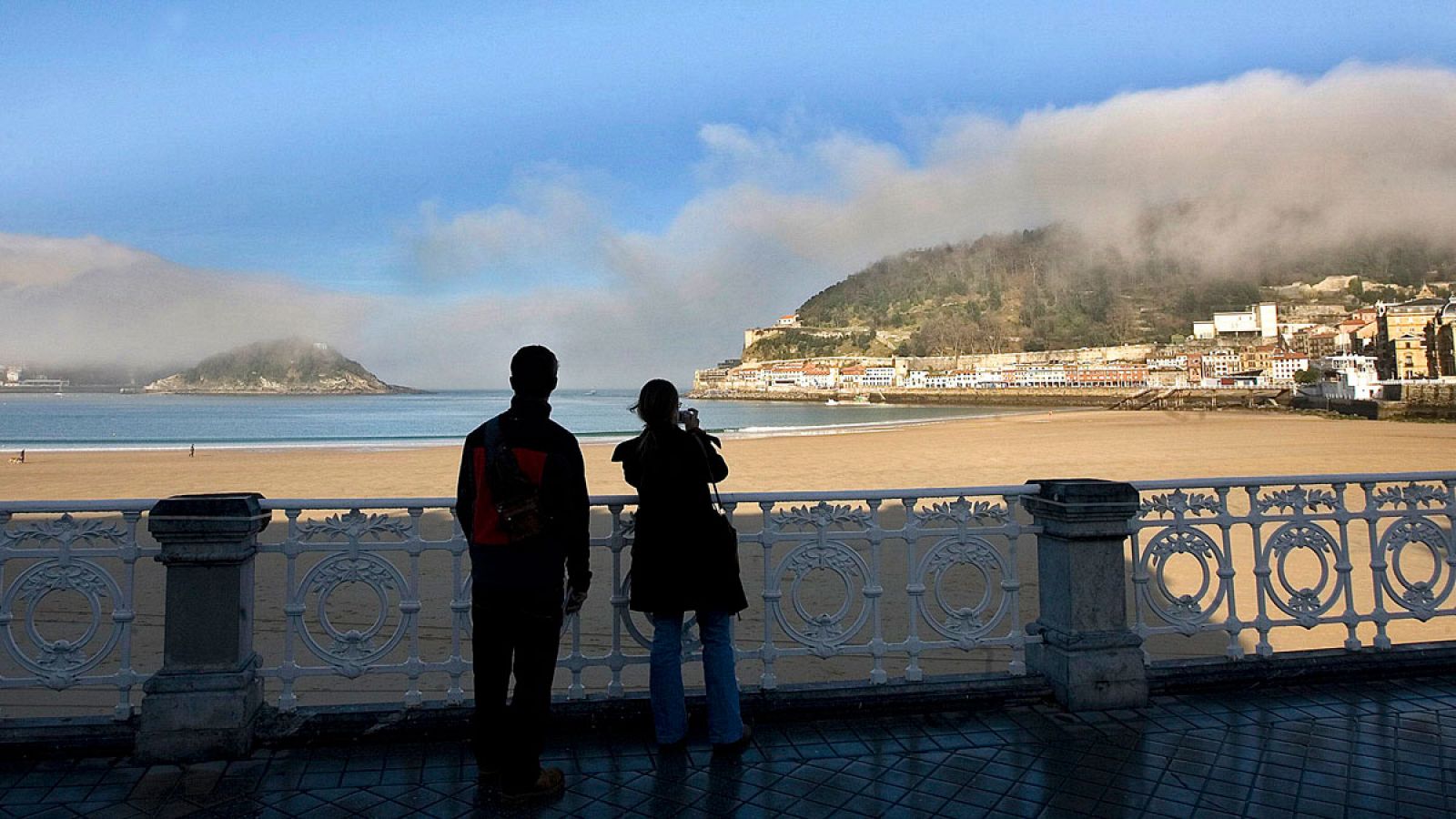 Fotografía de archivo que muestra a una pareja de turistas que toman una fotografía desde la playa de la Concha de San Sebastián