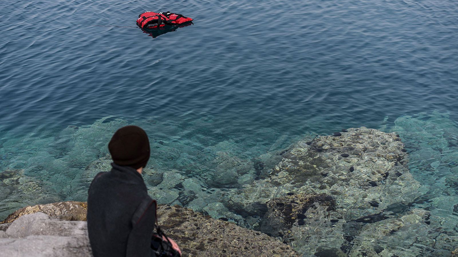 Un hombre observa un chaleco salvavidas en el mar Egeo desde el puerto turco de Dikili