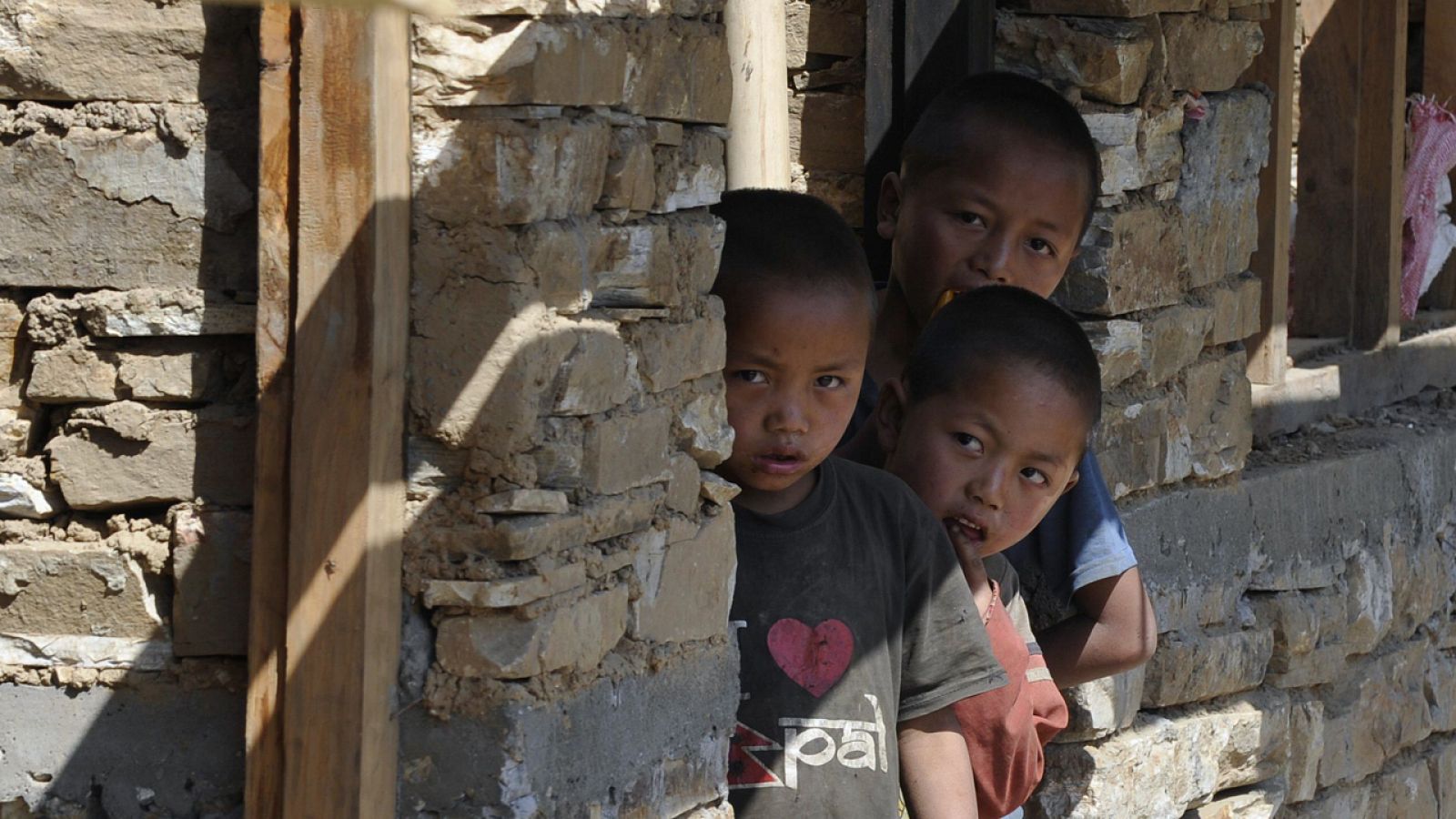 Niños nepalíes asoman por la ventana de una casa en construcción un año después del terremoto